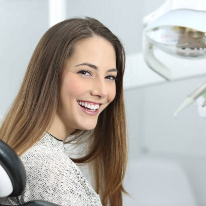 Satisfied dentist patient showing her perfect smile after treatment in a clinic box with medical equipment in the background